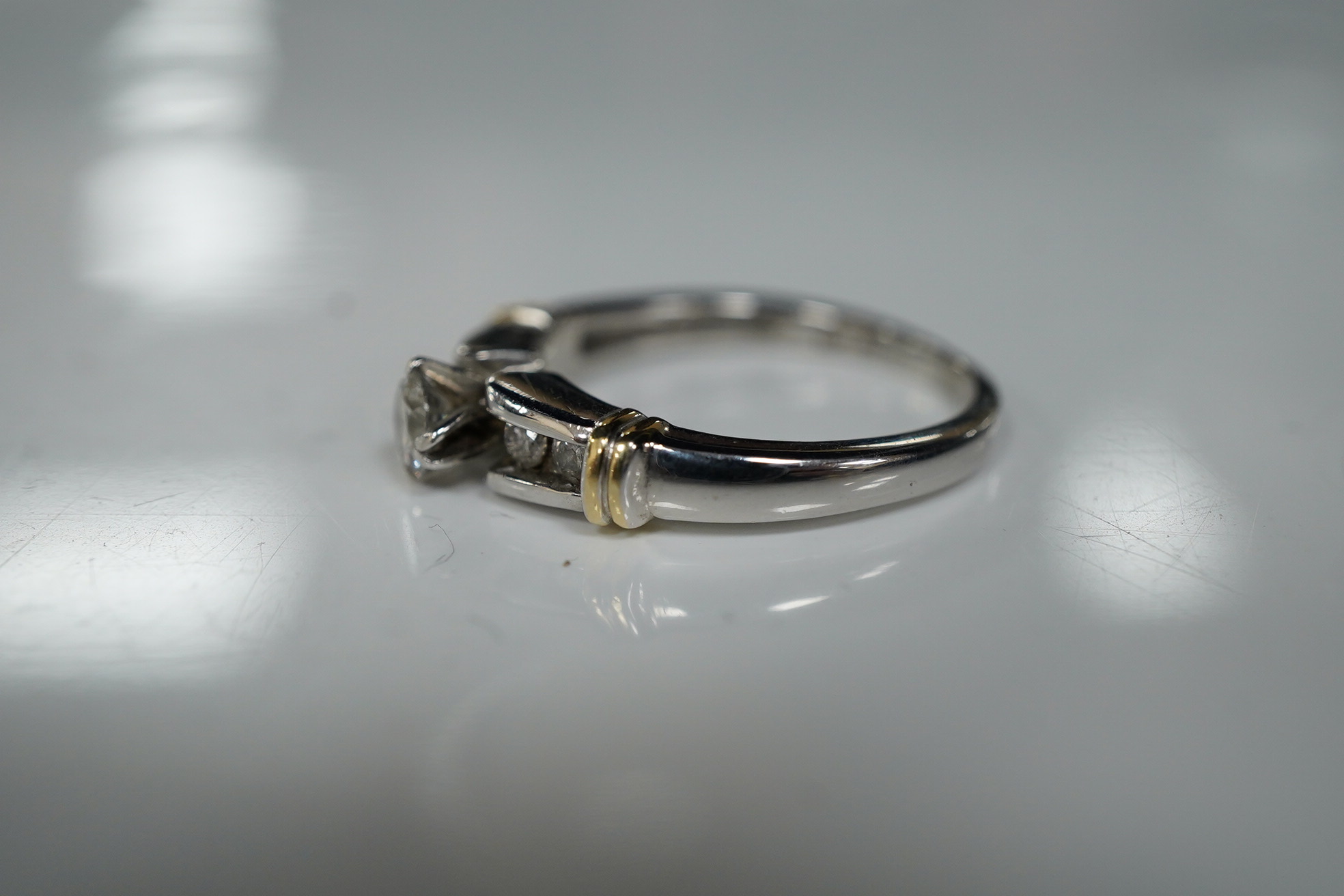 A diamond ring, claw-set with a brilliant-cut diamond weighing approximately 0.30 carats, to shoulders channel-set with smaller brilliant-cut diamonds, mounted in white gold, size R, stamped 14K, gross weight approximate